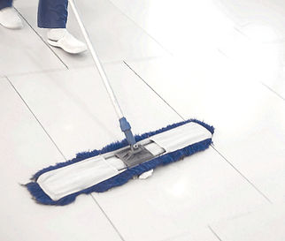 A commercial sweeping broom with a blue pad and white handle is being pushed over a white floor.