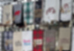 Display of hanging kitchen towels with animal and plaid designs, witty sayings like Beach Please and Got Wine?, in a craft market booth