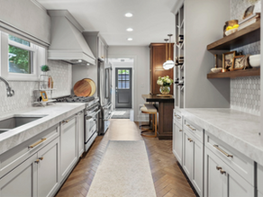 Modern kitchen with gray cabinets, marble countertops, herringbone wood floor, and hexagon tile backsplash. Bright and spacious.