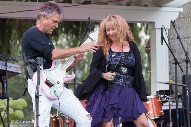 Male guitarist and red-haired singer perform on an outdoor stage, with drums and mic stands behind them.