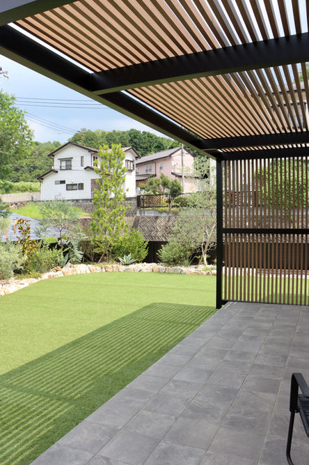 津山市の外構造園施工例:2025年~。造作パーゴラの縦格子が、タイルテラスと人工芝にドラマチックな影を描く庭
