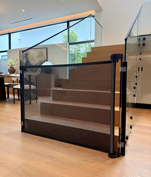 Retractable mesh baby safety gate installed at the bottom of a staircase with glass railing
