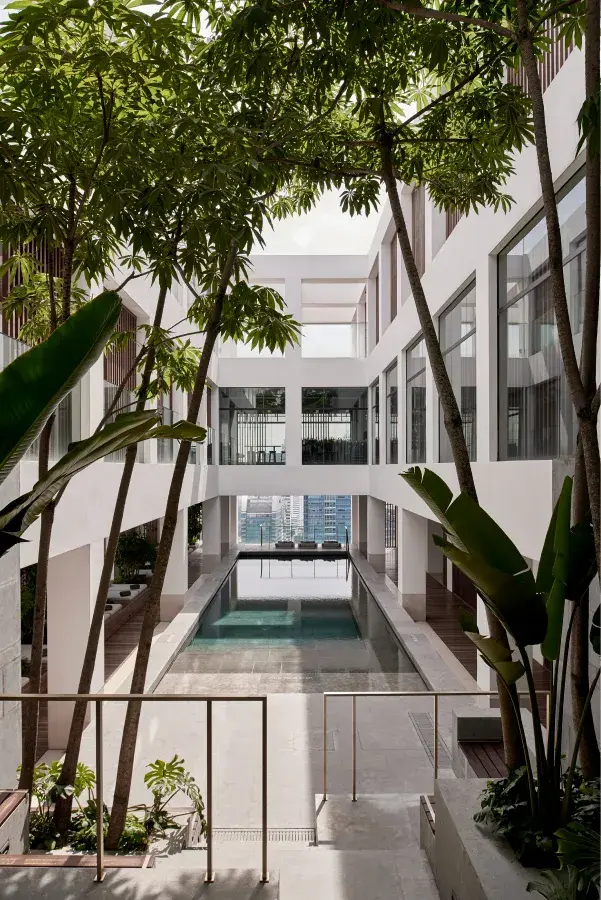 Pool in an atrium on a high floor of a hotel with trees surrounding and white walls.