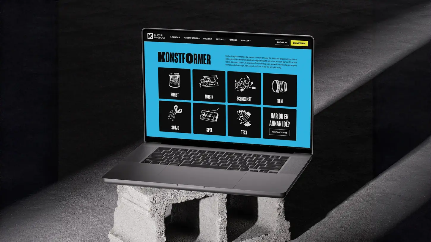 En svart laptop står upphöjd på två betongblock, belyst av ett mjukt, nästan dramatiskt ljus från sidan. Skärmen visar Kultur Ungdoms webbplats, med en modern, minimalistisk design. Bakgrunden på skärmen är ljusblå, och webbplatsen listar olika konstformer som "konst, musik, scenkonst, film, slöjd, spel, text" i svarta fyrkanter med vita ikoner som representerar varje kategori. Texten på hemsidan beskriver hur Kultur Ungdom stödjer unga kreatörer inom dessa områden genom vägledning och finansiering. Ljusets placering skapar starka skuggor som framhäver betongblockens grova struktur, och betongen står i kontrast mot datorns släta, moderna yta, vilket ger bilden en subtil balans mellan kreativt kaos och digital precision.