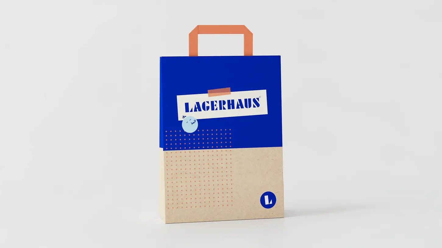 En blå och beige presentpåse med Lagerhaus logotyp och grafiska detaljer i orange och blått, designad för att se glad och lekfull ut.