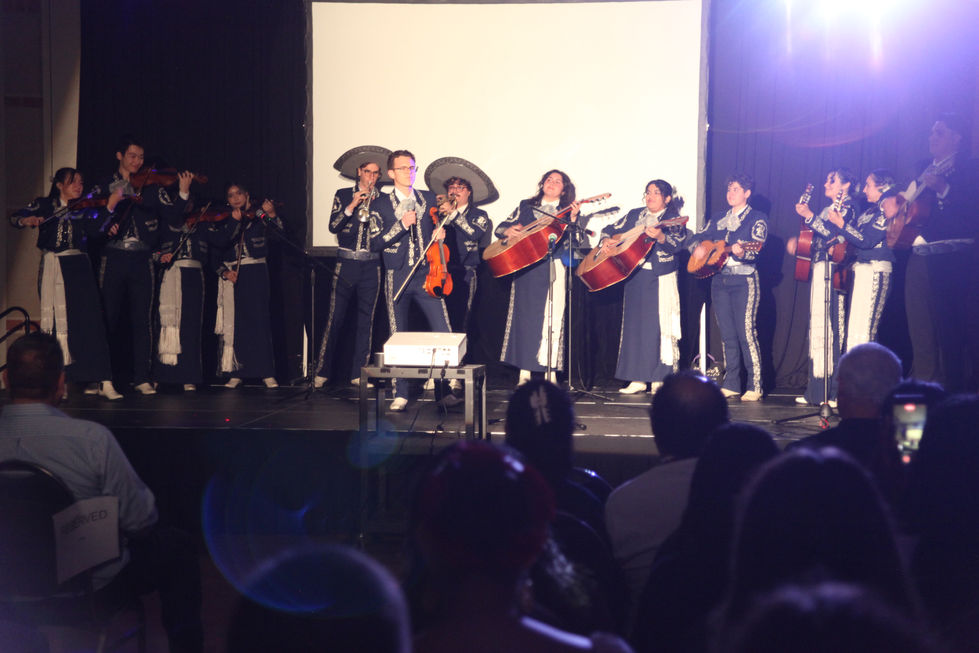 male singer holds a mic while the mariachi is in formation and plays behind him on stage