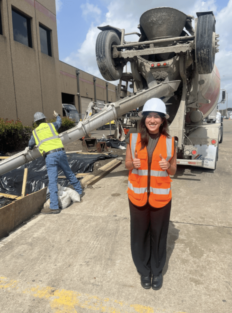 Nancy giving two thumbs up in an orange vest in front of a concrete truck