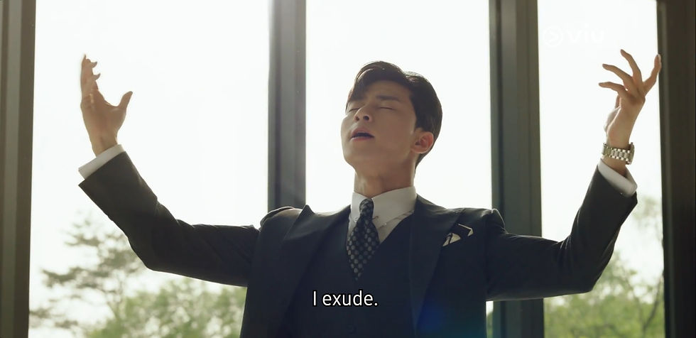 Man in a suit stands with arms raised, eyes closed, appearing confident. Bright window behind him. Subtitles read: I exude.