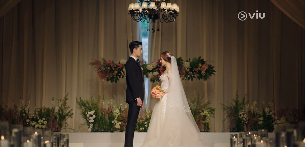 Bride and groom stand facing each other in a floral-decorated wedding venue. Bride holds peach roses. Emotional and elegant atmosphere.