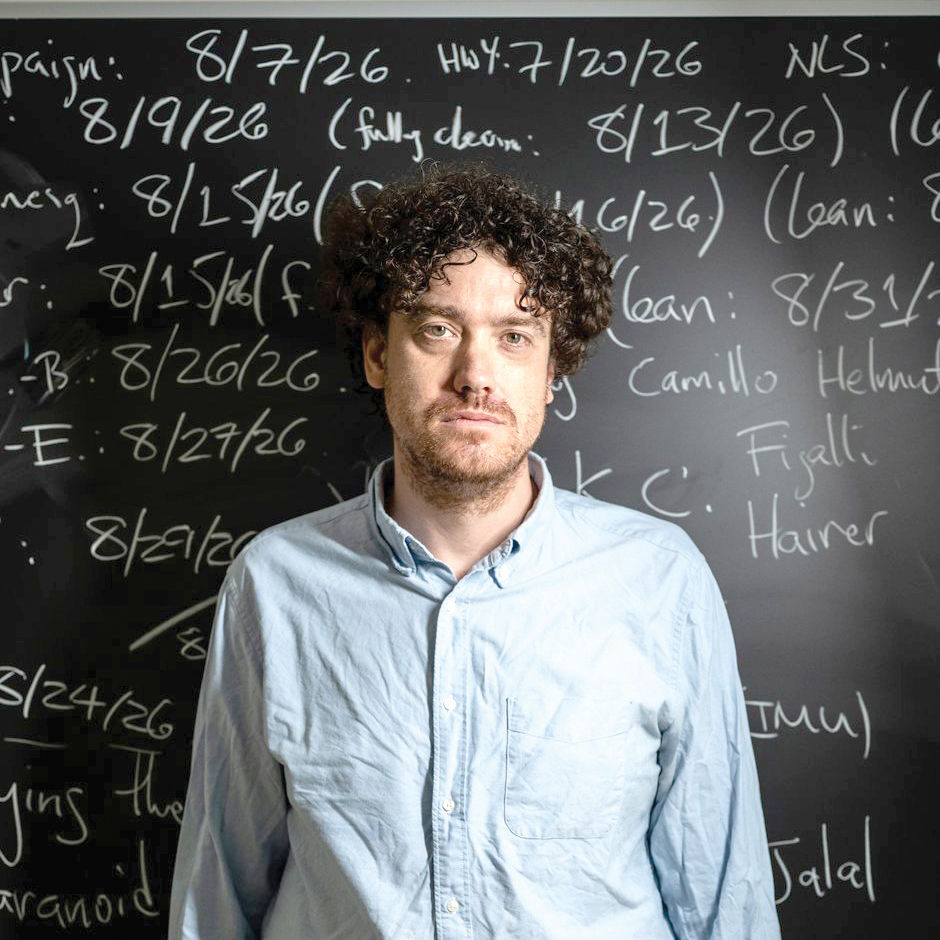 Tristan Buckmaster, a mathematician at New York University, stands in front of a chalkboard where he marked a timeline of events leading up to OpenAI’s announcement, and his own research progress, on solving the Navier-Stokes equations in New York on Sept. 9, 2026. Buckmaster was on the path toward an important proof when one of the artificial intelligence giants used its staggering resources to get there first. (Graham Dickie/The New York Times)