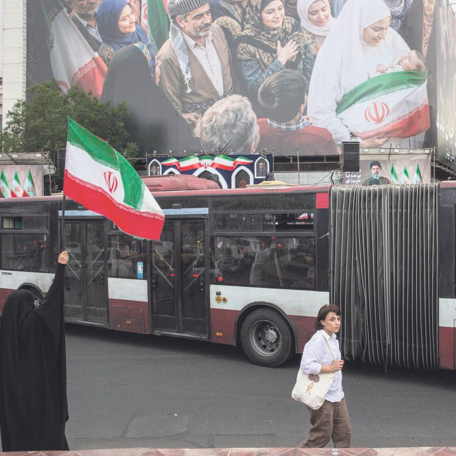 A woman waves an Iranian flag near a new billboard in Enghelab Square in Tehran, May 24, 2026. After devastating strikes and amid a teetering ceasefire, hopes entertained by some Iranian opponents of the Islamic Republic that the war would bring an end to decades of theocratic rule have been snuffed out. (Arash Khamooshi/Polaris for The New York Times)