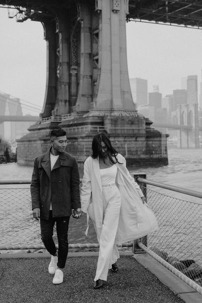 Black-and-white portrait of couple embracing beneath the Manhattan Bridge tower in DUMBO Brooklyn, NYC