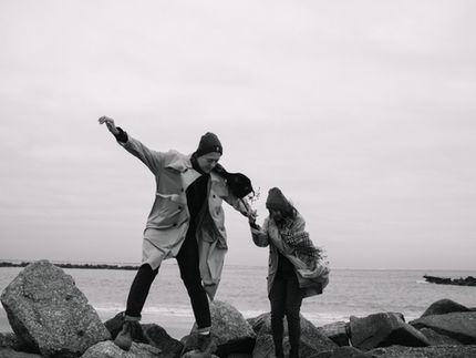 Black-and-white wide shot of couple dancing together on Coney Island beach in winter, rocks and ocean behind them, NYC