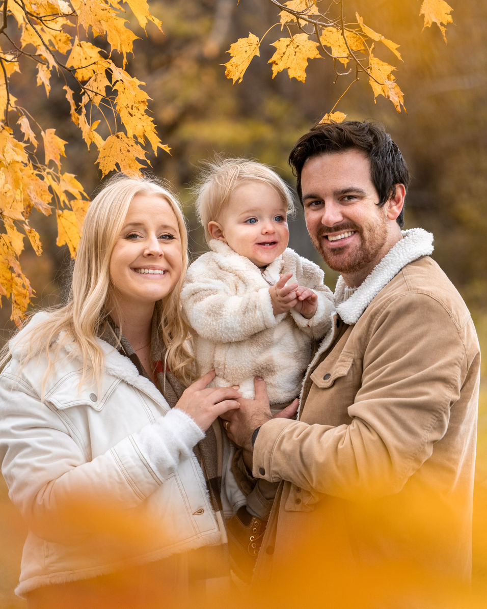 Smiling family posing outdoors in autumn leaves.