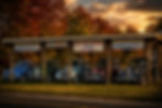 Row of restored vintage cars parked beneath a roadside auto shop canopy in Mena, Arkansas, surrounded by autumn trees and retro signage.