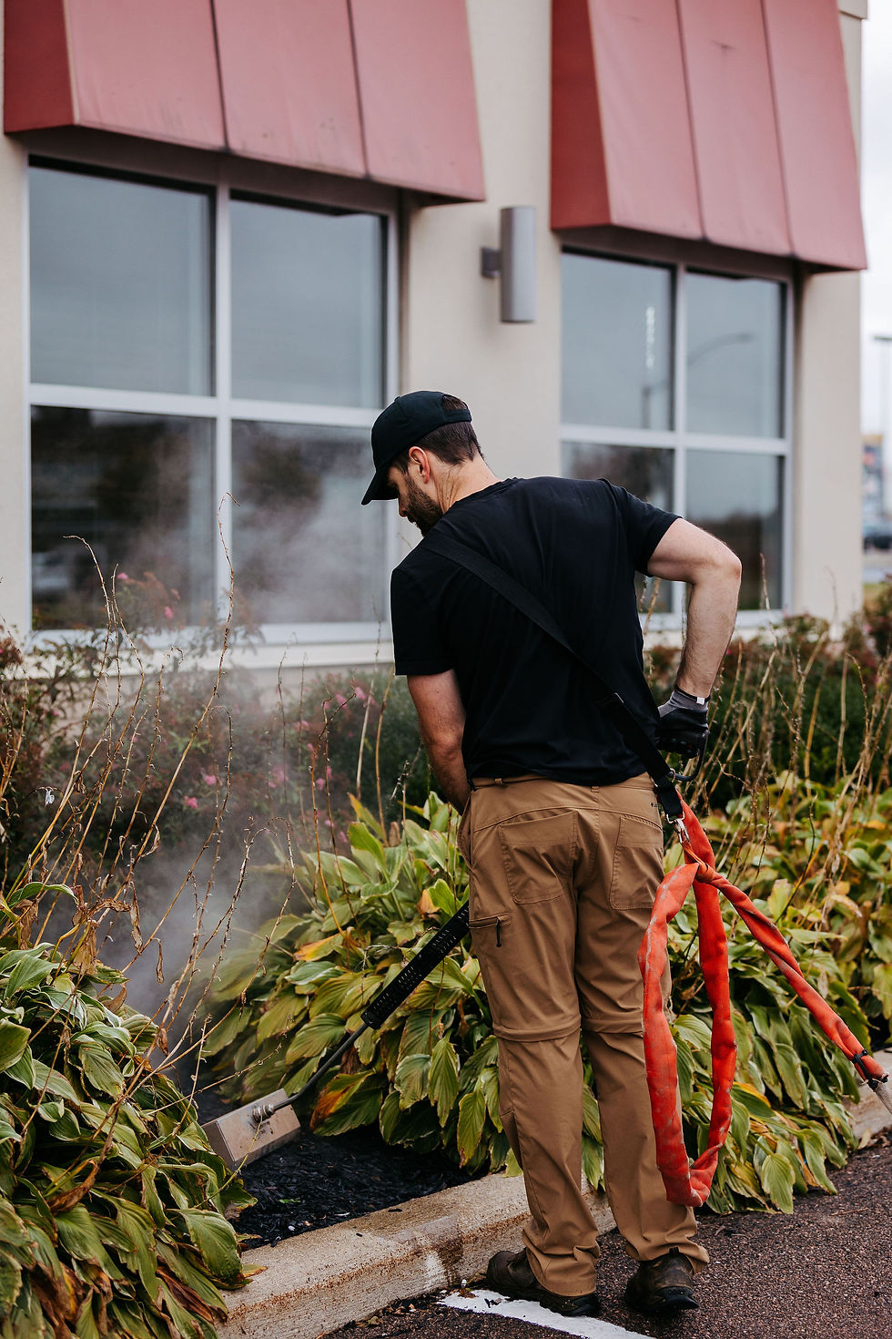 Technician using Satusteam™ superheated water system to control weeds around commercial landscaping beds beside a building.