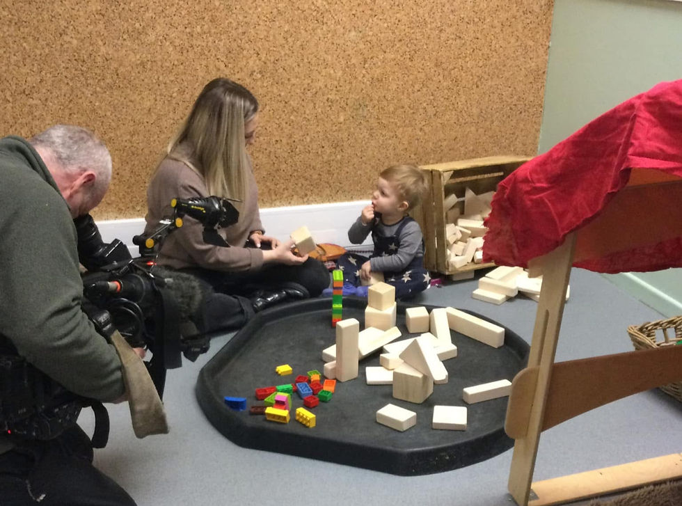 A lady sitting with a deaf child playing with blocks, with a cameraman filming for the news