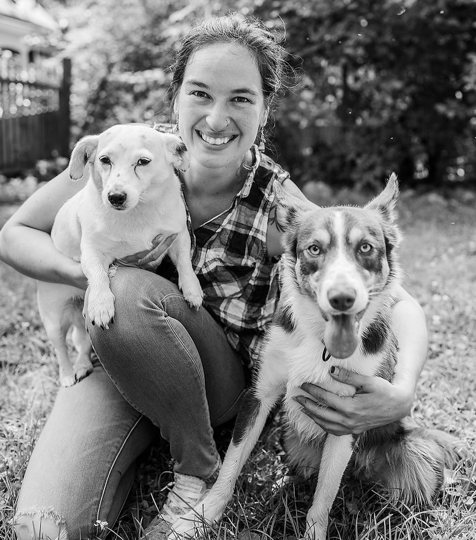 A woman kneeling with two dogs looking at the camera. The picture is black and white.