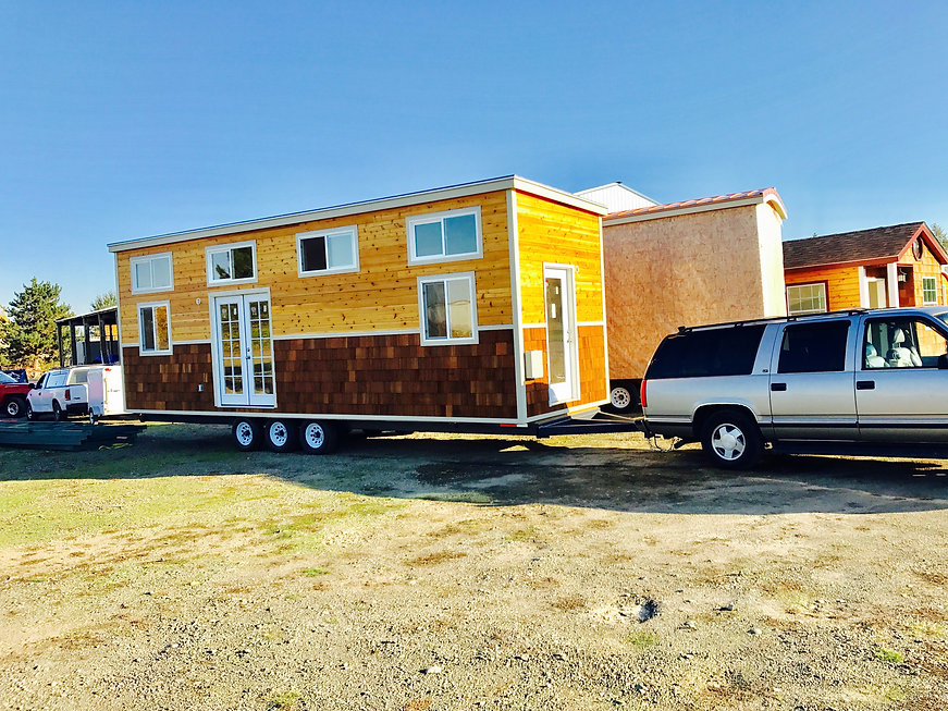 A tiny house on a trailer is being pulled by a suburban