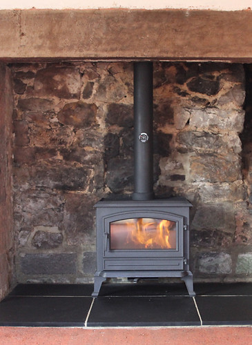Black stove fitted in a stone recess alongside installer headshot