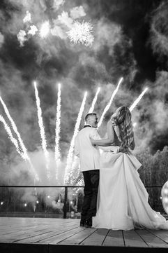 Bride and groom sharing a kiss as fireworks explode behind them.