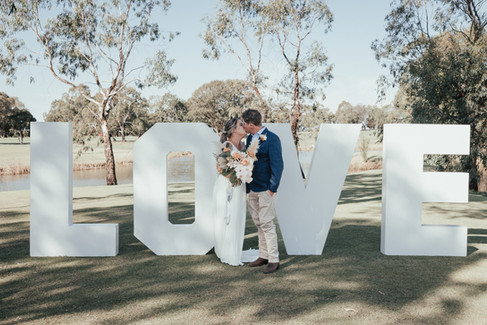 bride and groom kissing in front of large love letters
