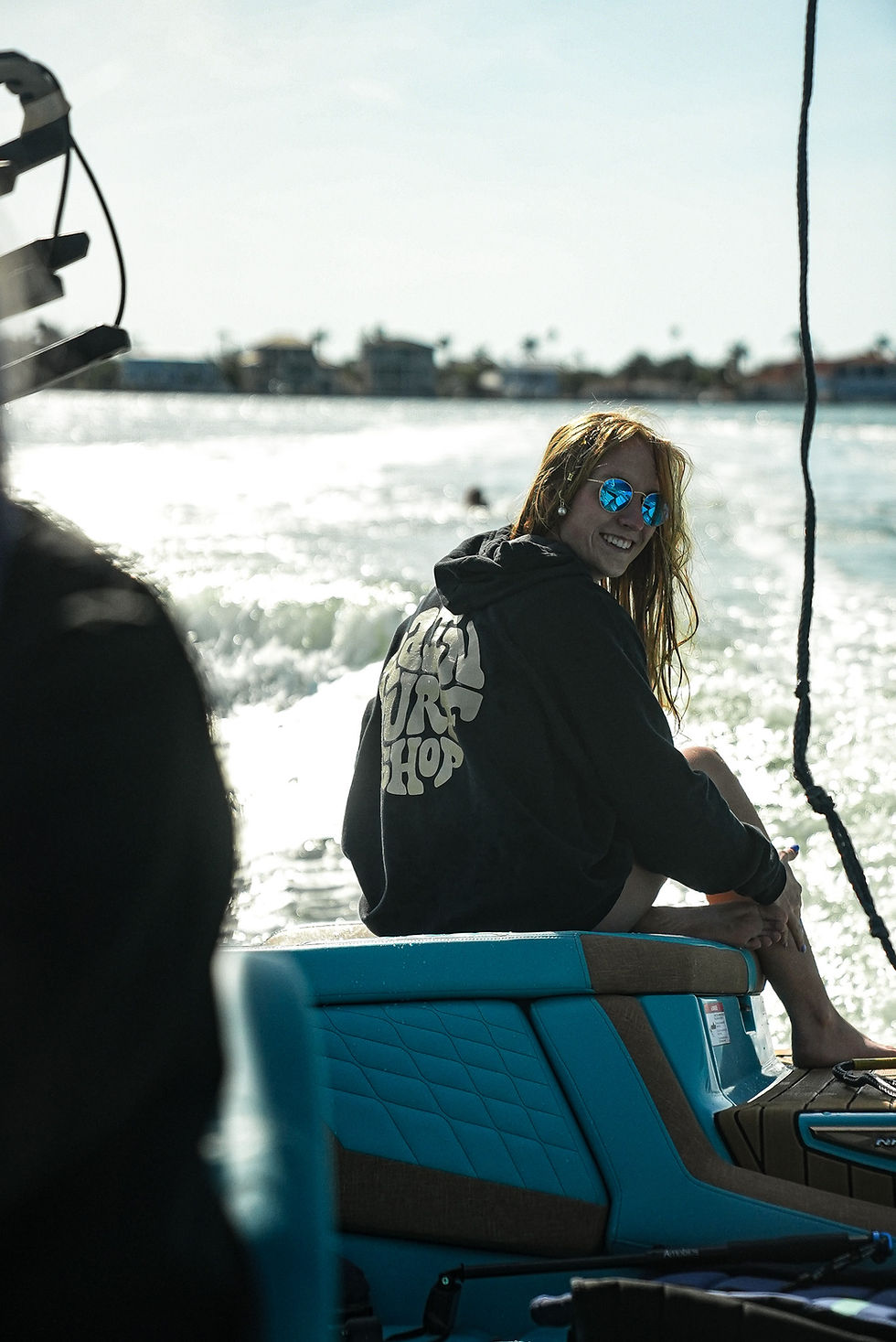 Girl on the back of a surf boat in a hoodie and sunglasses