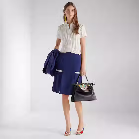 Thumbnail: Woman in white shirt, blue skirt, holding jacket and handbag