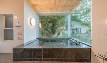 A black granite bathtub with a large window overlooking the forest.
