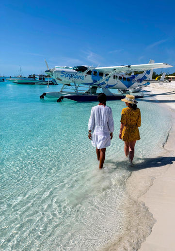 Two people walk towards a Seaplane Safaris aircraft parked at a beach in the Bahamas