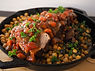 A cast iron skillet full of braised pork shoulder on a bed of chickpeas