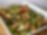 A dish of chicken strips in sauce topped with cut pieces of scallions and red chilis