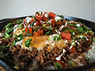 A cast iron skillet of taco rice topped with ground beef, diced tomatoes, cilantro and crema 