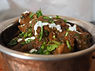 A bowl of lamb curry garnished with yogurt sauce and cilantro