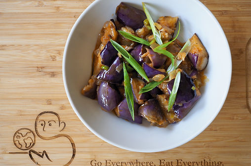 Top view of Sichuan Eggplant garnished with scallions. Text, "Go Everywhere, Eat Everything"