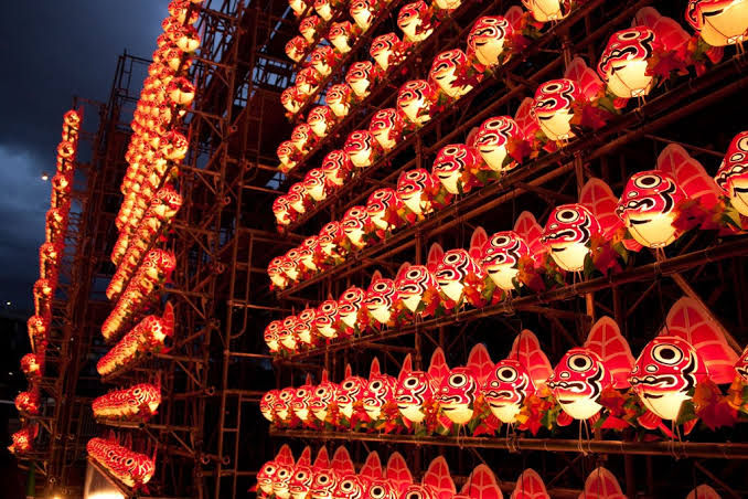 Rows of glowing red lanterns with face designs on scaffolding at night, creating a festive, crowded display.