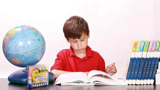 A boy studying on a study table surrounded by books pencils