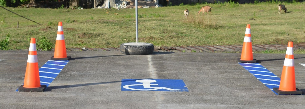 Ein markierter Rollstuhl-Piktogrammplatz auf Asphalt, flankiert von vier orange-weißen Verkehrshütchen, die einen Parcours abgrenzen.