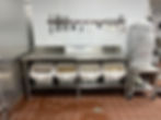 commercial kitchen stainless steel prep station with mounted knives and ingredient storage bins
