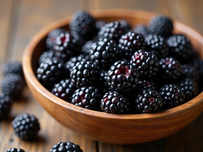a close up of freshly picked blackberries in a wooden bowl