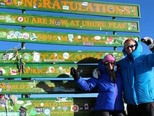 Martin Ingjerd stands at Uhuru Peak on Mount Kilimanjaro with a companion, in front of the summit sign. The photo highlights adventure, teamwork, and taking on challenges.