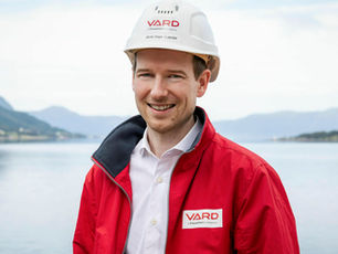 Arnt Inge Gjerde wearing a VARD hard hat and red jacket, standing by the fjord.
