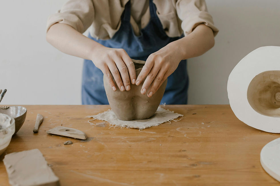 Hands shaping a clay pot on a wooden table during a relaxed at-home pottery session.