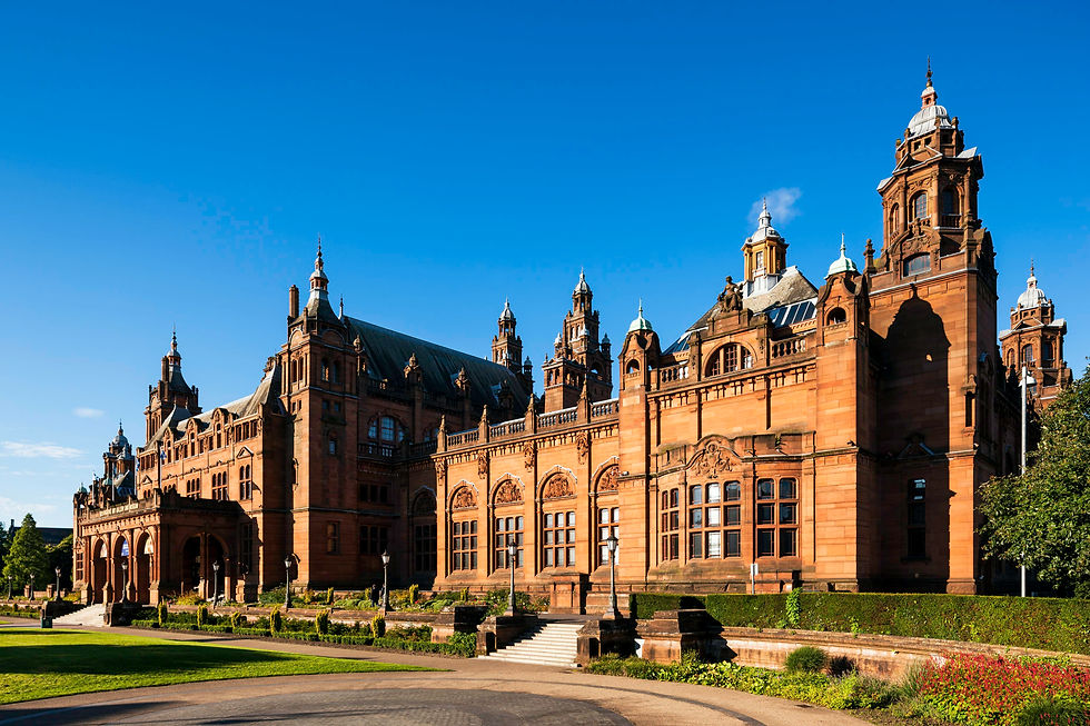 Historic, ornate building with towers against a clear blue sky. Red-brown stone facade, arched windows, lush gardens, serene mood.