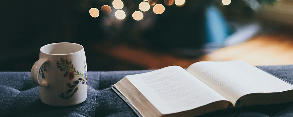 A cozy scene with an open Bible and floral mug on a sofa, set against a background of blurred warm lights, evoking a peaceful mood.