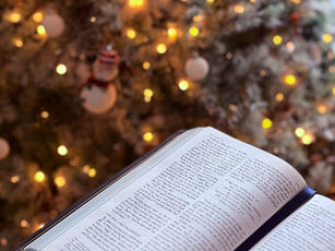 A cozy scene with an open Bible and floral mug on a sofa, set against a background of blurred warm lights, evoking a peaceful mood.