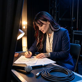 Female professional rewriting part of her speech by hand at a small backstage table moments before walking onstage.