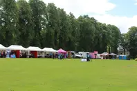 Outdoor event with stalls and tents, people walking, green grass, and trees. Renfrew Community Co