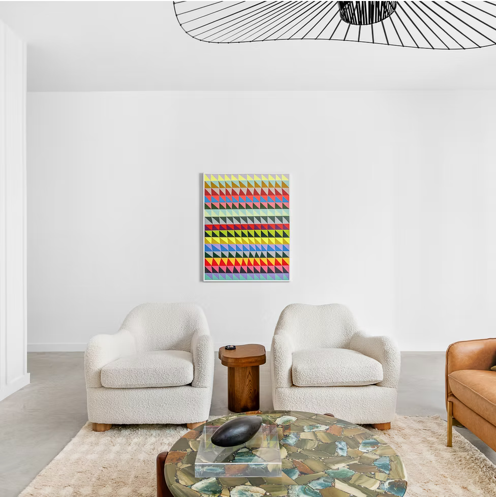 White arm chairs against a white wall with a colorful, geometric art piece centered between them
