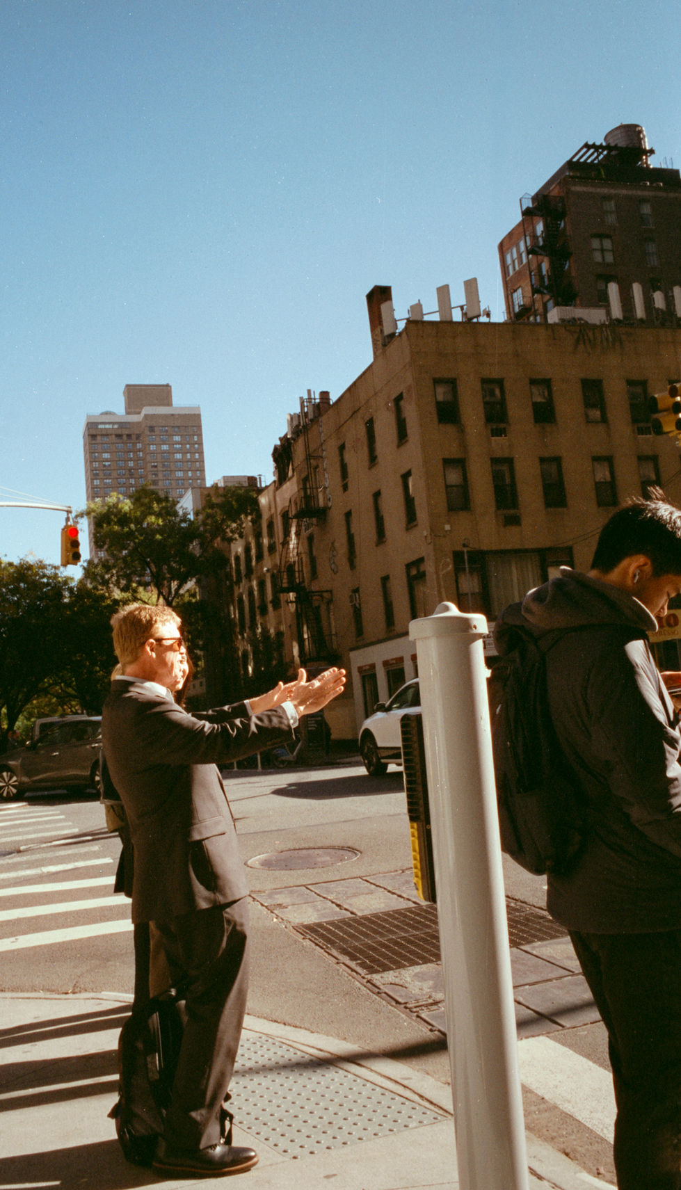 Man in suit pointing up on a sunny city street corner.